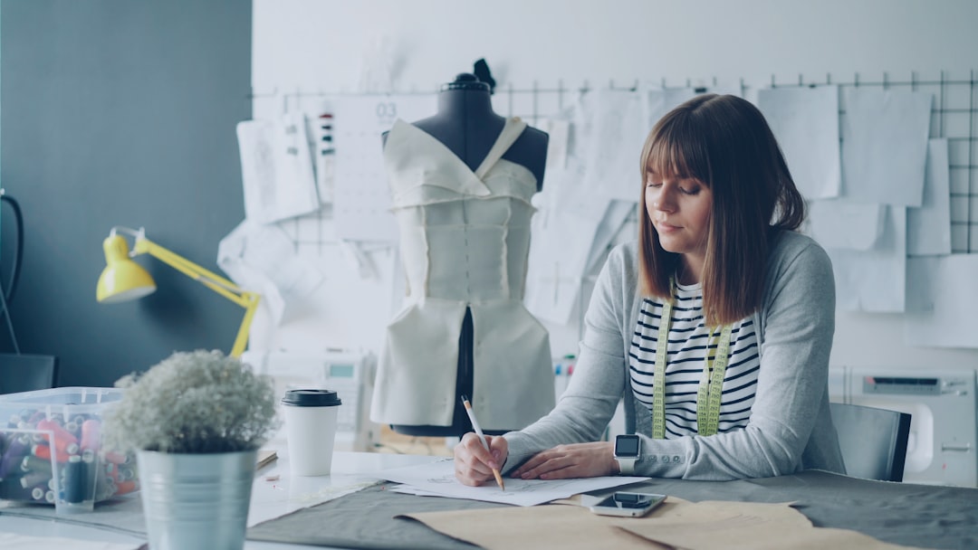 Attractive clothing designer in small start-up business is drawing sketches for womens clothes and thinking about next fashion show. Inspiration and creative thinking concept.